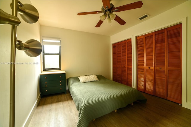 bedroom with hardwood / wood-style flooring, ceiling fan, and multiple closets