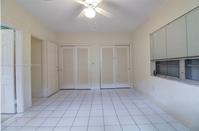 unfurnished bedroom with ceiling fan, light tile patterned floors, and two closets