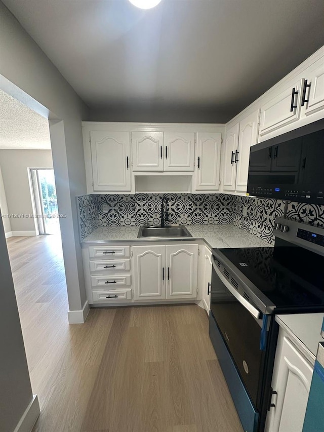 kitchen with sink, white cabinets, backsplash, light hardwood / wood-style floors, and black / electric stove