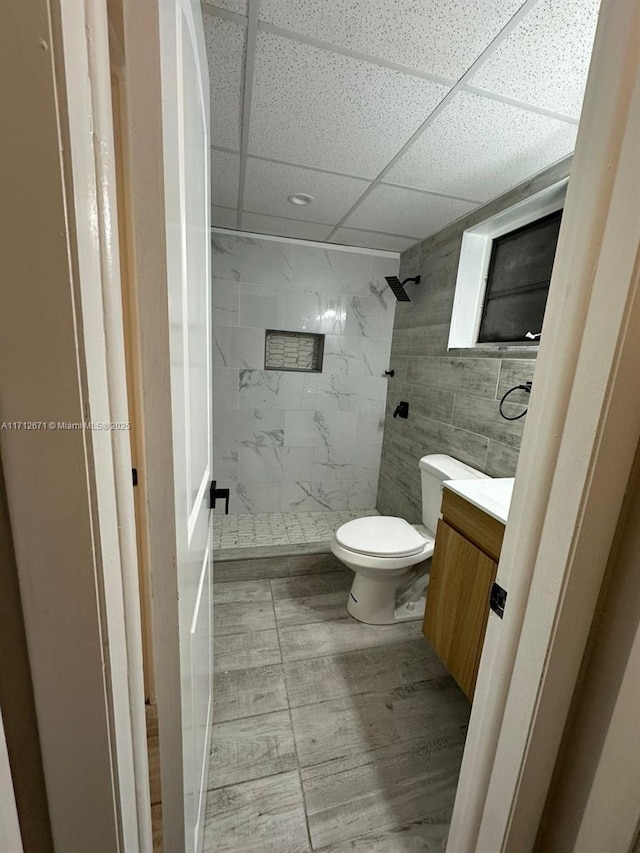 bathroom featuring tile walls, tiled shower, vanity, a drop ceiling, and toilet