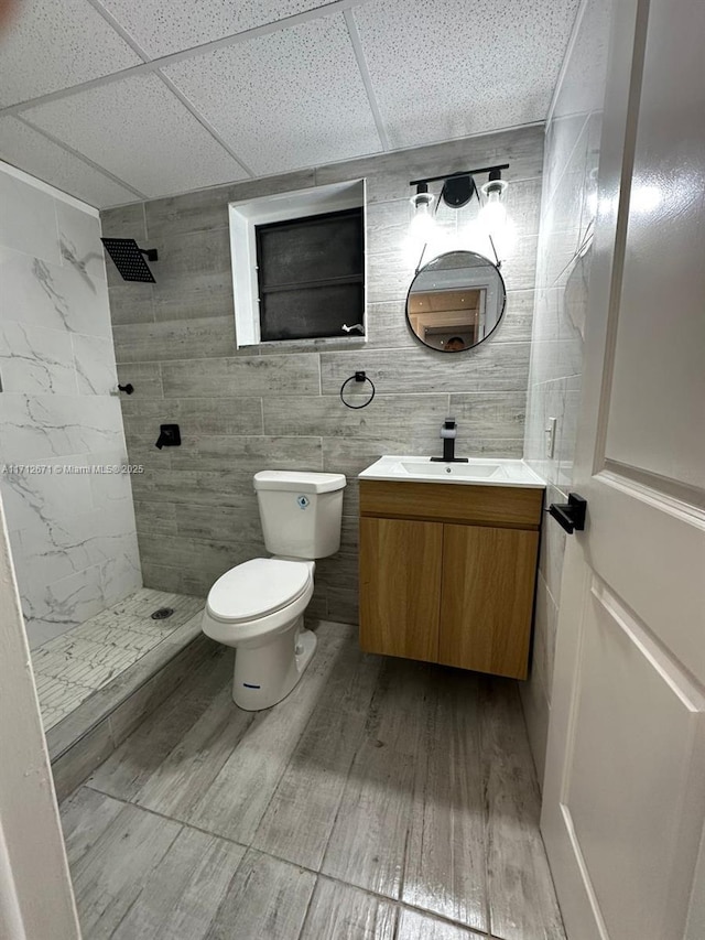 bathroom featuring a tile shower, a paneled ceiling, vanity, and toilet