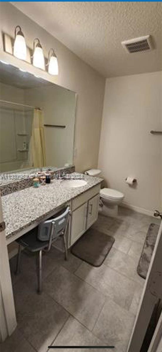 bathroom with tile patterned floors, a textured ceiling, vanity, toilet, and curtained shower