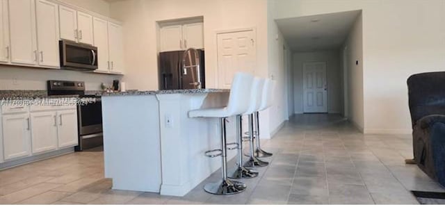 kitchen featuring white cabinets, stone counters, stainless steel appliances, and a breakfast bar area