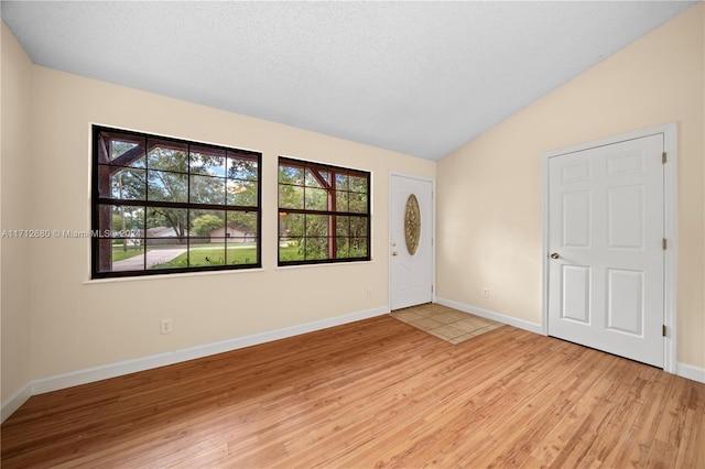 entrance foyer with light hardwood / wood-style floors, a textured ceiling, and vaulted ceiling