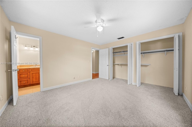 unfurnished bedroom with ensuite bathroom, ceiling fan, light colored carpet, and multiple closets