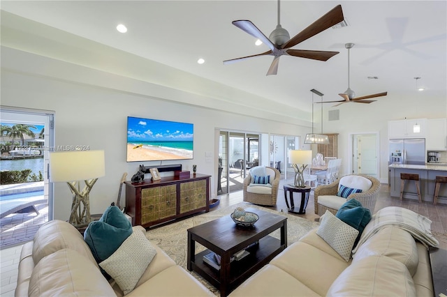 living room with ceiling fan with notable chandelier, light wood-type flooring, and a high ceiling