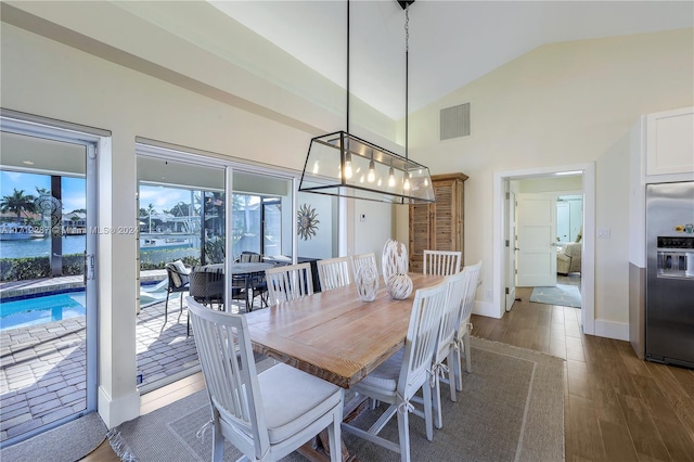 dining room featuring dark hardwood / wood-style flooring, a water view, and vaulted ceiling