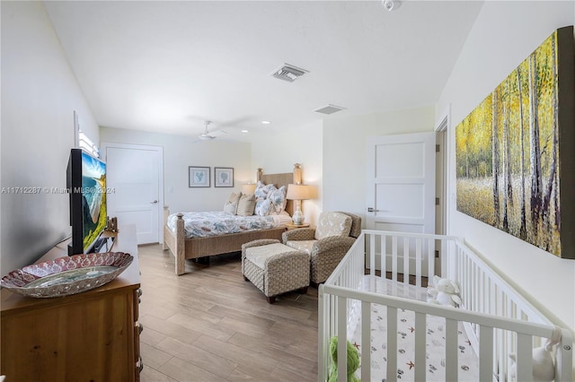 bedroom with hardwood / wood-style floors, ceiling fan, and a nursery area