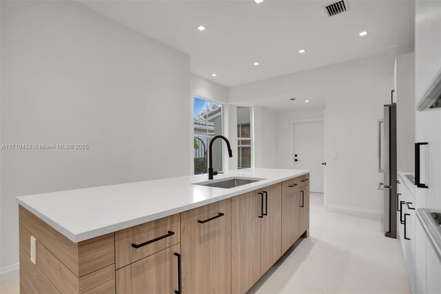 kitchen with light brown cabinets, a center island, stainless steel refrigerator, and sink