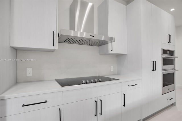 kitchen with white cabinetry, stainless steel double oven, wall chimney range hood, and black electric cooktop