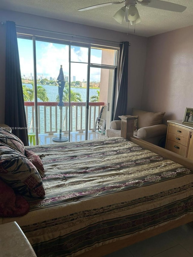 bedroom featuring tile patterned floors, a textured ceiling, access to outside, ceiling fan, and a water view