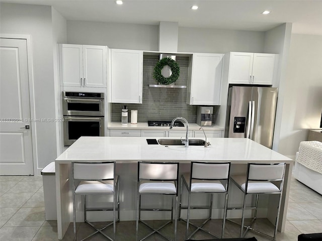 kitchen with a kitchen breakfast bar, a center island with sink, white cabinets, and appliances with stainless steel finishes