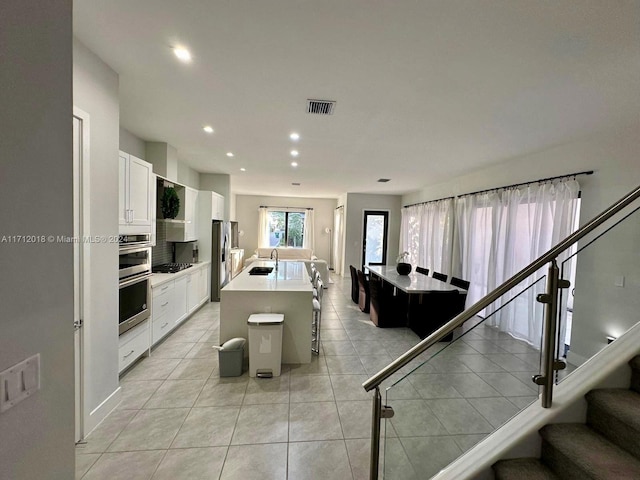 kitchen with a breakfast bar, a kitchen island with sink, white cabinets, sink, and light tile patterned flooring