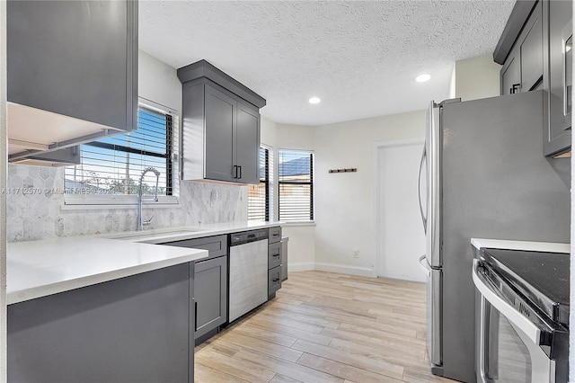 kitchen with decorative backsplash, light wood-type flooring, stainless steel appliances, sink, and gray cabinets