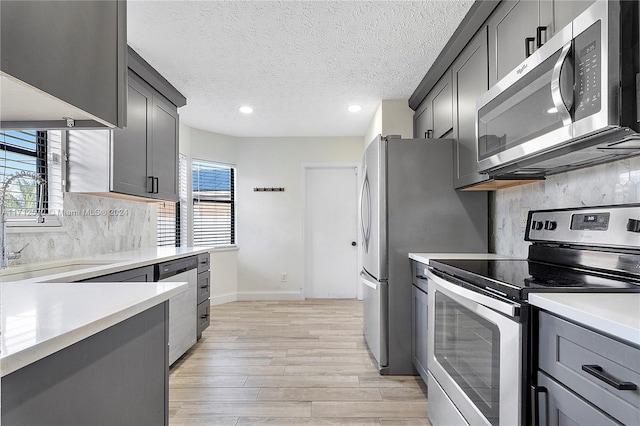 kitchen with gray cabinetry, backsplash, light hardwood / wood-style flooring, a textured ceiling, and stainless steel appliances