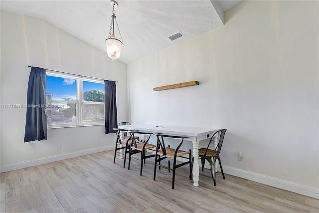 dining room featuring a textured ceiling, light hardwood / wood-style flooring, and lofted ceiling