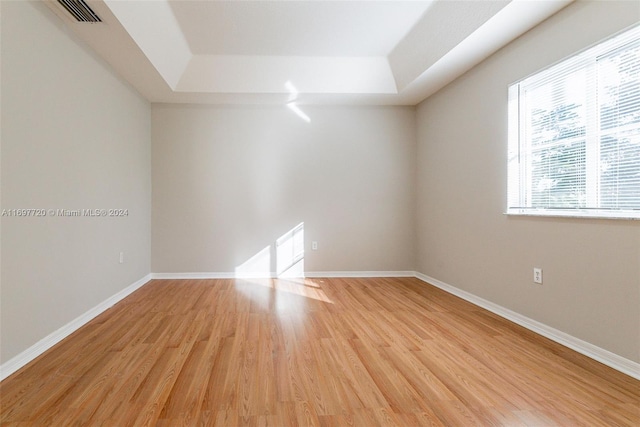 empty room with light wood-type flooring and a tray ceiling