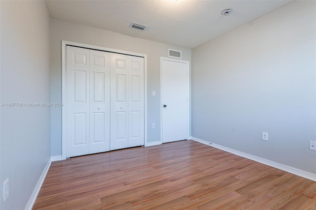 unfurnished bedroom with a textured ceiling, light hardwood / wood-style floors, and a closet