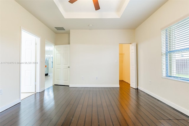 spare room with ceiling fan with notable chandelier, a raised ceiling, and dark wood-type flooring