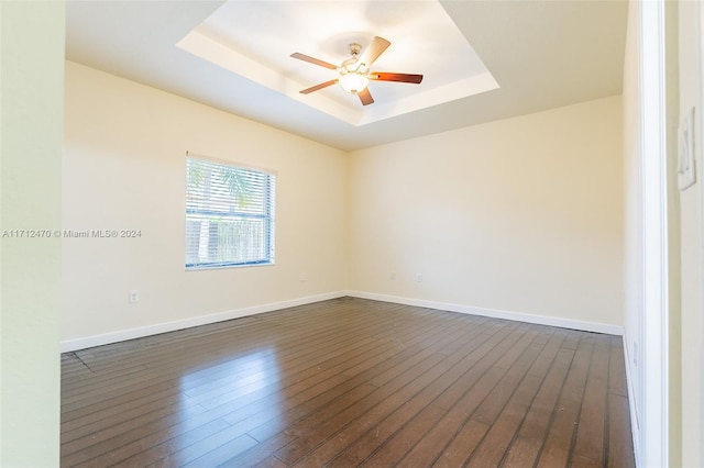 spare room featuring a raised ceiling, ceiling fan, and dark hardwood / wood-style flooring