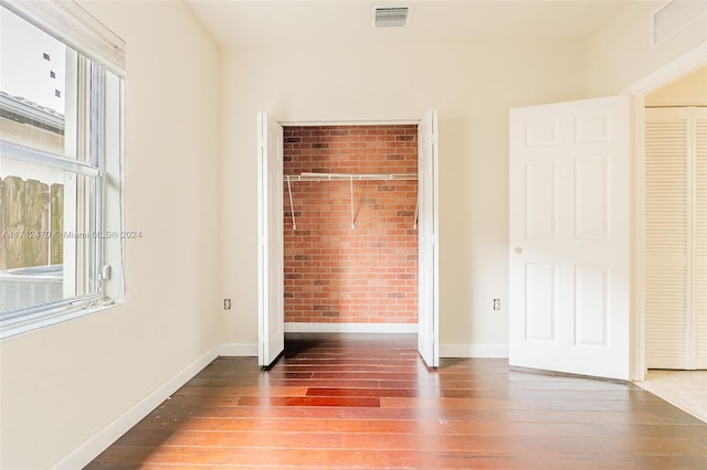 unfurnished bedroom with wood-type flooring, brick wall, and a closet