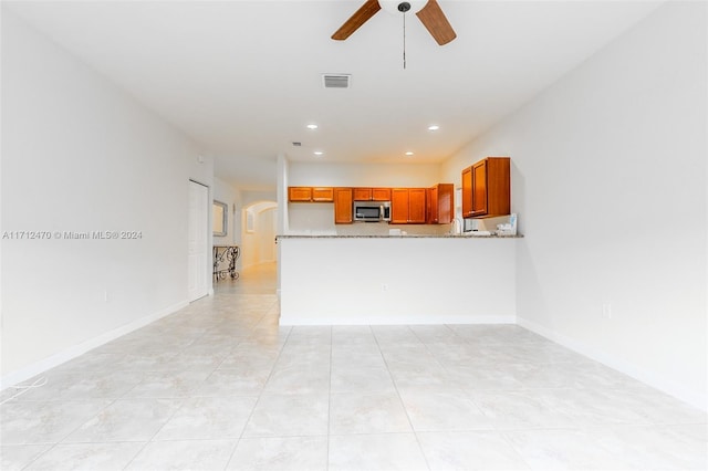 kitchen featuring kitchen peninsula, light tile patterned floors, light stone counters, and ceiling fan