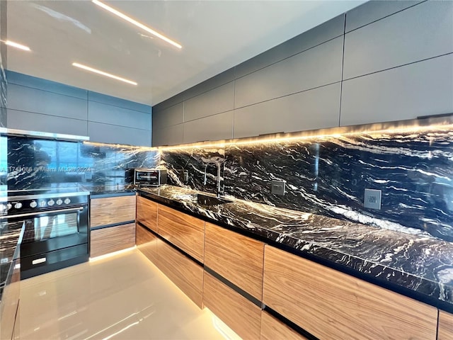 kitchen with decorative backsplash, dark stone countertops, sink, and black range with electric cooktop