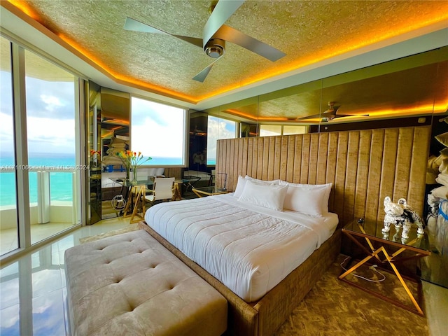 bedroom with a textured ceiling, a water view, ceiling fan, and wood walls