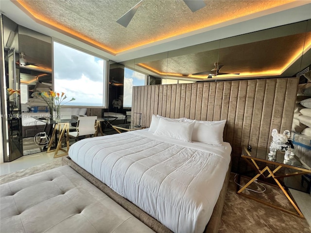 bedroom featuring a raised ceiling, ceiling fan, wooden walls, and a textured ceiling