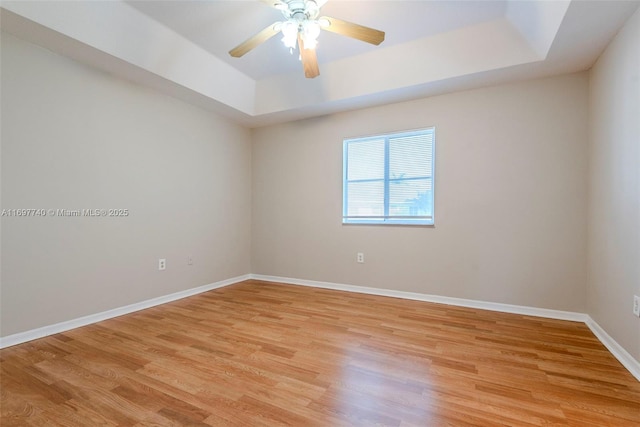 spare room featuring ceiling fan, light wood-type flooring, a raised ceiling, and baseboards