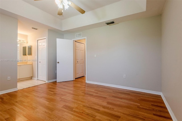 unfurnished bedroom featuring visible vents, light wood-style flooring, ensuite bathroom, and baseboards