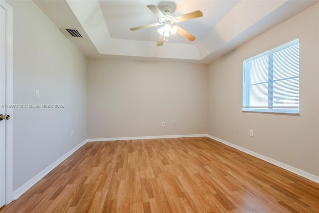 spare room with a raised ceiling, baseboards, visible vents, and light wood finished floors