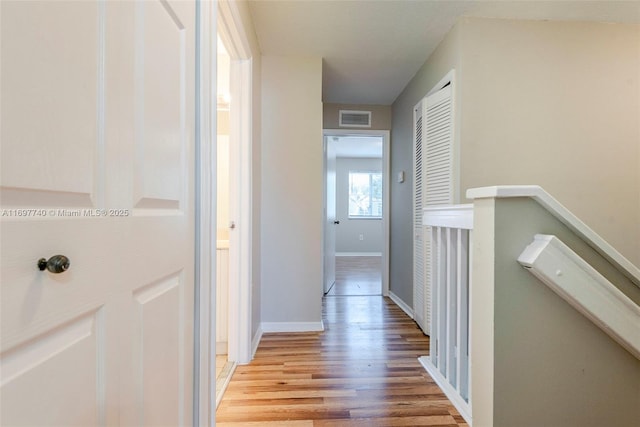 corridor with light wood-type flooring, visible vents, baseboards, and an upstairs landing