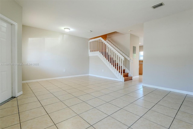 empty room featuring light tile patterned floors, visible vents, baseboards, and stairway