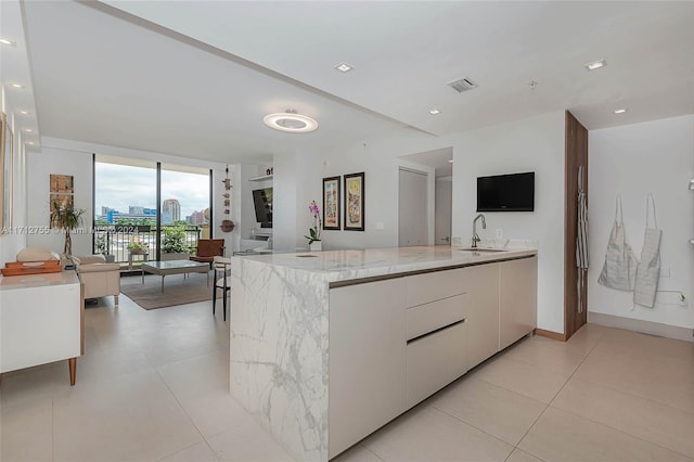 kitchen featuring kitchen peninsula, light stone counters, sink, white cabinets, and light tile patterned flooring