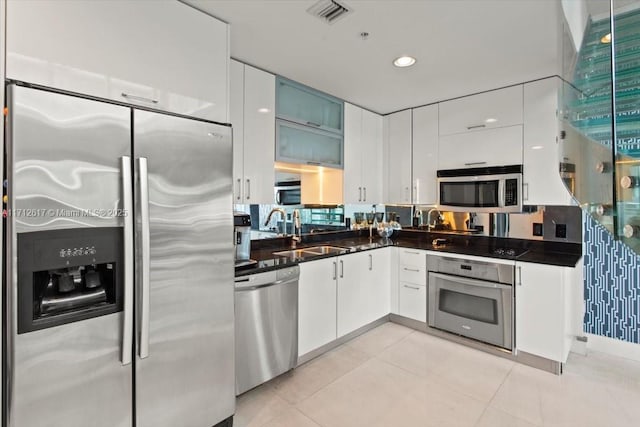 kitchen with appliances with stainless steel finishes, light tile patterned floors, white cabinetry, and sink