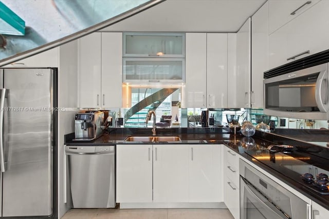 kitchen with white cabinets, stainless steel appliances, dark stone counters, and sink