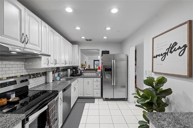 kitchen featuring stainless steel appliances, dark stone counters, white cabinets, decorative backsplash, and light tile patterned flooring