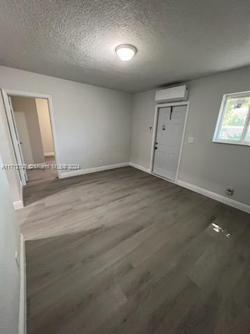 empty room featuring dark hardwood / wood-style flooring, a textured ceiling, and a wall mounted AC