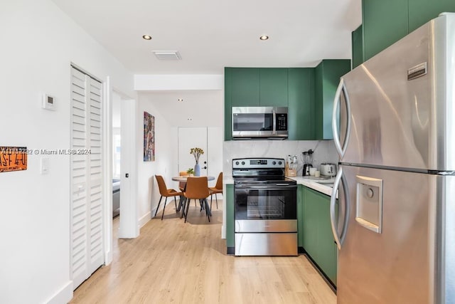 kitchen with decorative backsplash, green cabinets, light wood-type flooring, and stainless steel appliances