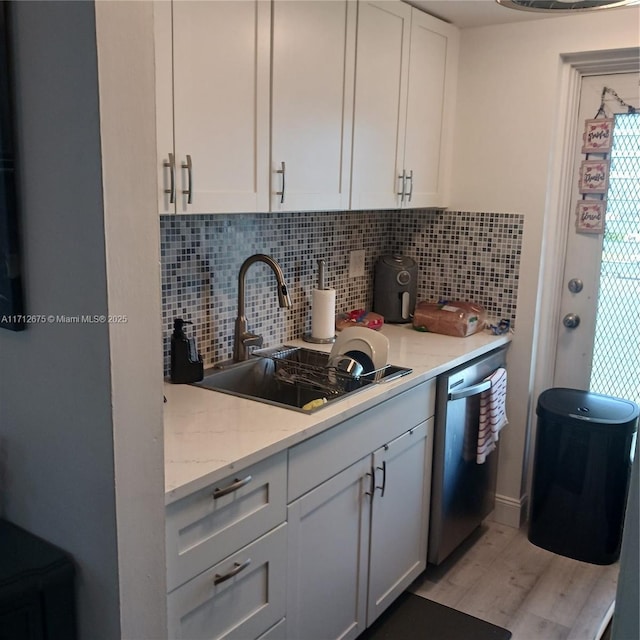 kitchen featuring decorative backsplash, stainless steel dishwasher, a sink, light wood-style floors, and white cabinets