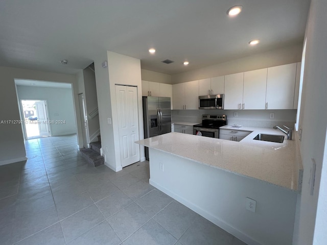 kitchen featuring white cabinetry, sink, light stone counters, kitchen peninsula, and appliances with stainless steel finishes