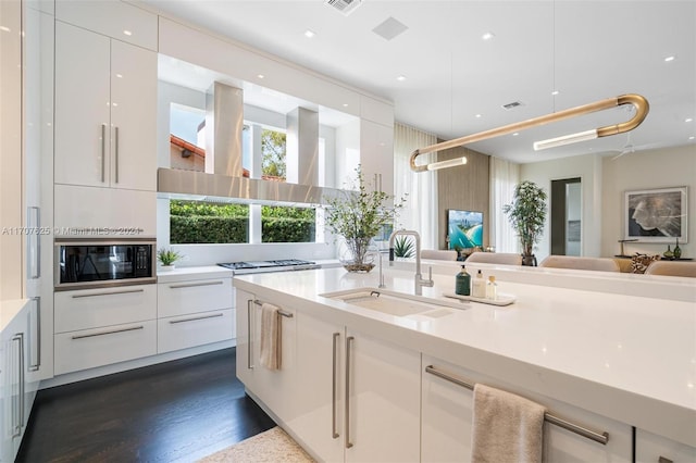 kitchen with stainless steel gas stovetop, white cabinetry, black microwave, dark hardwood / wood-style flooring, and sink