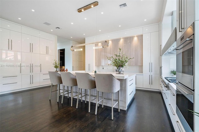 kitchen with decorative light fixtures, white cabinetry, a kitchen breakfast bar, dark hardwood / wood-style floors, and a large island