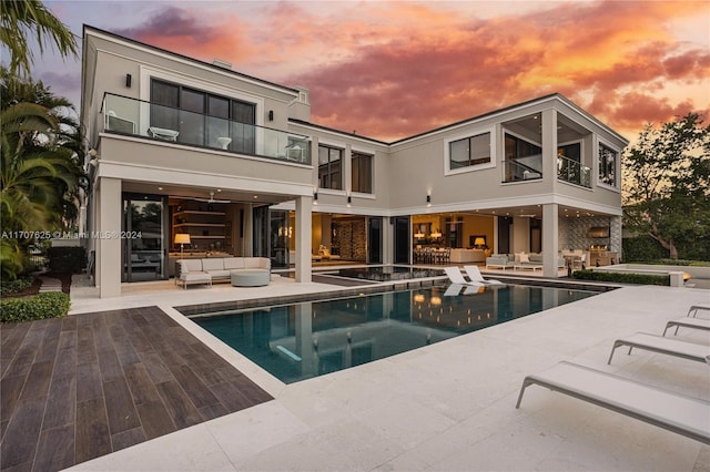 back house at dusk featuring a pool with hot tub, an outdoor hangout area, and a patio area