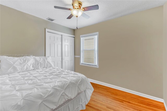 bedroom with ceiling fan, a closet, a textured ceiling, and hardwood / wood-style flooring