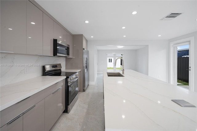 kitchen with gray cabinetry, light stone counters, sink, and stainless steel appliances