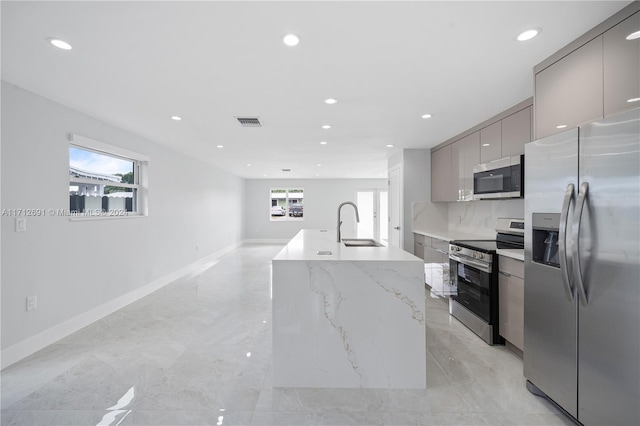 kitchen featuring gray cabinetry, a kitchen island with sink, sink, light stone countertops, and stainless steel appliances