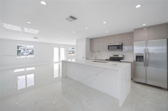 kitchen featuring sink, stainless steel appliances, backsplash, gray cabinets, and a center island with sink