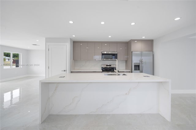 kitchen featuring light stone countertops, appliances with stainless steel finishes, gray cabinetry, sink, and a large island